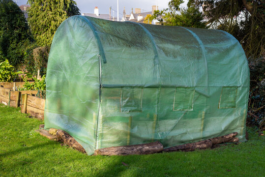 Large protective net greenhouse with roll-up windows and door in vegetable garden with planters.
