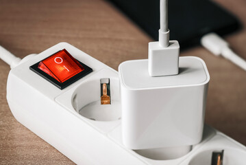 A charger adapter with a USB cable connected to a power supply with a red switch for charging a...