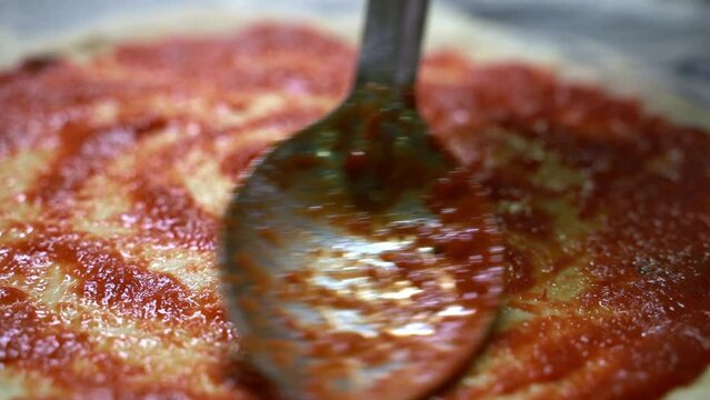 Metal spoon applying a tomato sauce on a pizza dough to make a pizza in slow motion