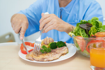 Asian senior or elderly old lady woman patient eating breakfast and vegetable healthy food with hope and happy while sitting and hungry on bed in hospital.
