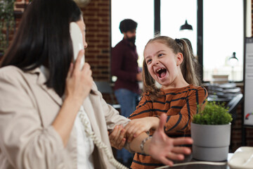 Busy businesswoman trying to talk on telephone while screaming and annoying daughter disturbs her...