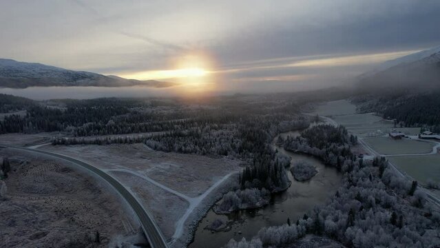 Flying over foggy icy treetops and frozen fields at sunset in Northern Scandinavia Helgeland, Northern Norway. Arial shot over Bl&aring;fjelldalen, ascending flyover drone shot.