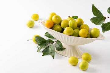 yellow freshly torn cherry plum with green leaves in a ceramic vase on a white background
