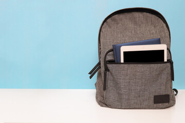 Backpack with notebook and tablet in pocket on wooden table. Blue wall background. Back to school...