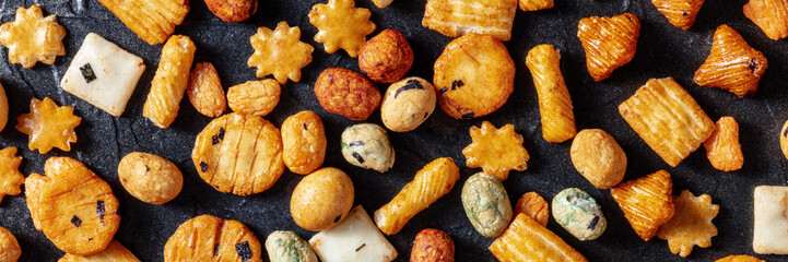 Japanese crackers on a black slate background, overhead flat lay panoramic banner