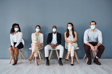 Fototapeta na wymiar The precautions we take now will ensure our safety and success. Portrait of a group of businesspeople wearing face masks while sitting in line against a grey background.
