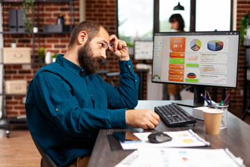 Fototapeta na wymiar Focused pensive entrepreneur sitting at table thinking at project ideas working at marketing strategy planning business presentation. Concentrated businessman analyzing data charts in startup office