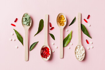 Top view Variety of vitamin and mineral pills in wooden spoon on Colored background. Top view of...