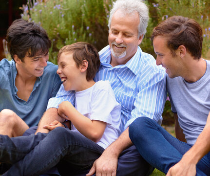 Bonding with my boys. Father and sons laughing with one another sitting on a lawn.