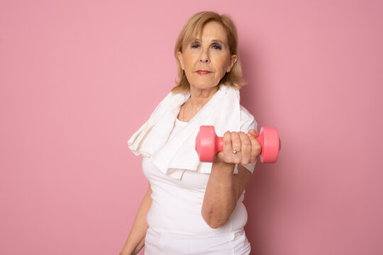 Smiling sport mature woman holding dumbbell isolated on pink background. Active senior lifestyle concept.