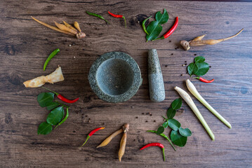 thailand spices around a Granite mortar and pestle. spice for made  curry paste ingredient together with tropical herbs on wood background at top view angle. Chili, kaffir lime leaves, lemongrass.