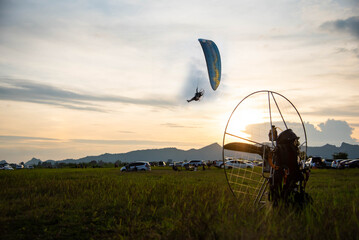 paraglider fly with paramotor flying in the air on a sunset with an Mountain and horizon in the background with a giant sun - 491216691