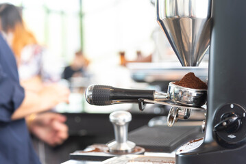 close up of coffee grinder grinding freshly roasted make beans into a powder, barista holding portafilter with ground coffee in cafe