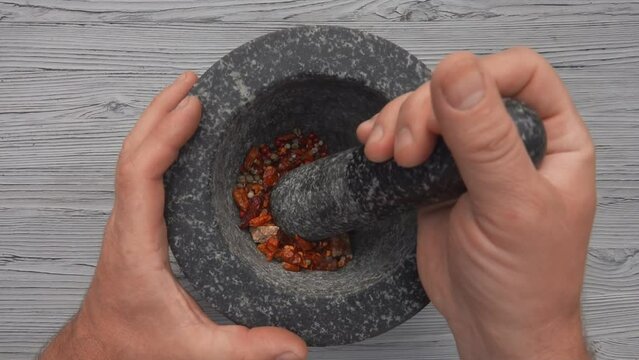 Top view of hand with heavy pestle starting to grind mix of spices and peppers