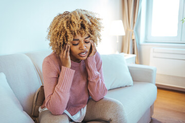 Frustrated woman suffering from the headache while sitting on the sofa at home. Feeling bad. Young...
