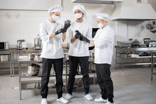 Team of chefs wearing protective gloves and face masks, preparing for a job on the restaurant kitchen. Concept of new rules for business to prevent the spread of infections during pandemic