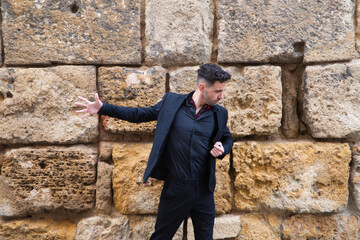 gypsy man dancing flamenco, young and handsome dressed in black and red shoes is posing and dancing on a background of a stone wall. Flamenco cultural heritage of humanity