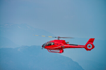 Red rescue helicopter flying in a mountain environment.