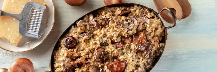Risotto ai funghi panorama, mushroom and cheese rice panoramic banner, with ingredients, overhead flat lay shot on a wooden background