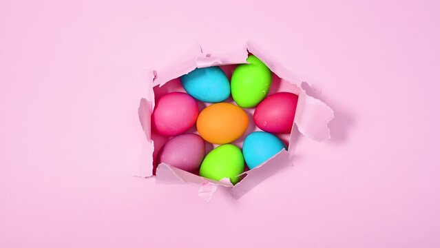 Tearing up pastel pink background with colorful Easter eggs under. Creative holidays stop motion