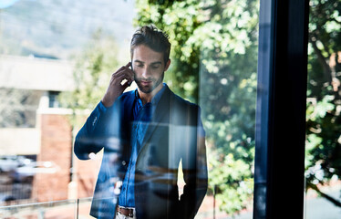 Taking care of business. Shot of a young businessman talking on the phone outside an office.