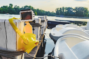 Close-up Waterproof action camera with yellow float and mask for snorkeling, diving weighs on a pole on a wooden pier. Against the backdrop of the pier.