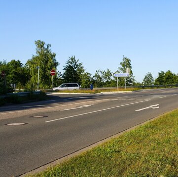 View of empty road in Itzehoe, Germany with traffic direction sign to Hamburg and trees in clear blue sky background. No people.