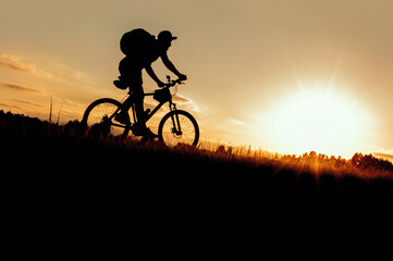 Fototapeta na wymiar Silhouette, a cyclist rides down a hill at sunset in the evening. concept of travel and adventure cycling tourists.