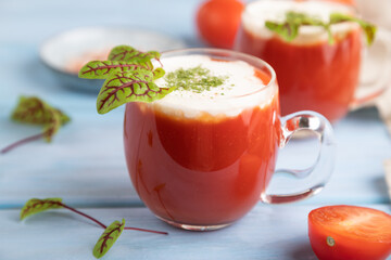 Tomato juice with sorrel, salt and sour cream in glass on blue wooden background. Side view, selective focus.