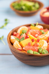 Vegetarian fruit salad of pumpkin, tangerine, pomegranate, microgreen sprouts on blue, side view, selective focus.