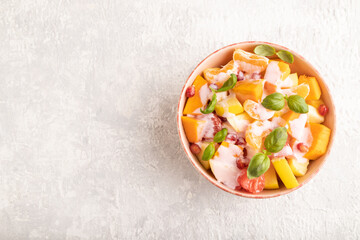 Vegetarian fruit salad of yogurt pumpkin, tangerine, basil microgreen on gray, top view, copy space.