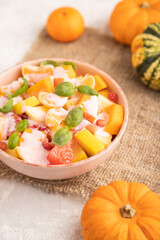 Vegetarian fruit salad of yogurt pumpkin, tangerine, basil microgreen on gray, side view, selective focus.