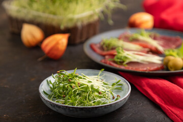 Slices of smoked salted meat with cilantro microgreen on black. Side view, selective focus.