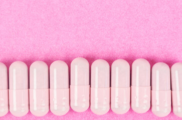 Pink capsule pills on pink background with copy space.