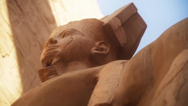 Close up of a statue of King Ramses in the Karnak Temple, Luxor Egypt. 
Slow camera rotation from a low angle, backlit by the sun. 