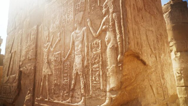 Close up of intricate carvings in the stone of a pillar in Karnak Temple, Luxor Egypt. 
Slow rotation around the corner of the pillar with light flare. 