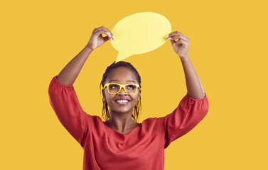 Studio shot of happy black woman teacher in glasses holding mock up thinking or speech bubble card,...