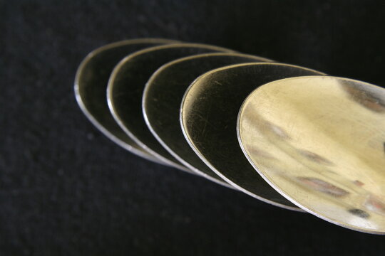 Cucharas de acero inoxidable para distintas preparaciones de  comida,  escalonadas con luz rasante que forman brillos en sus bordes,presenta un bello dise&ntilde;o abstracto con fondo negro