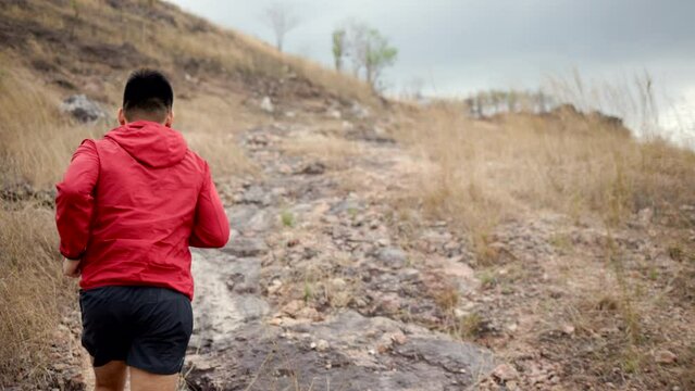 Smart trail runner man checking smart watch on rocky mountain. Athlete jog, exercising outdoor for healthy. Confident and powerful marathon man running workout and cardio. Sport and Lifestyle concept.