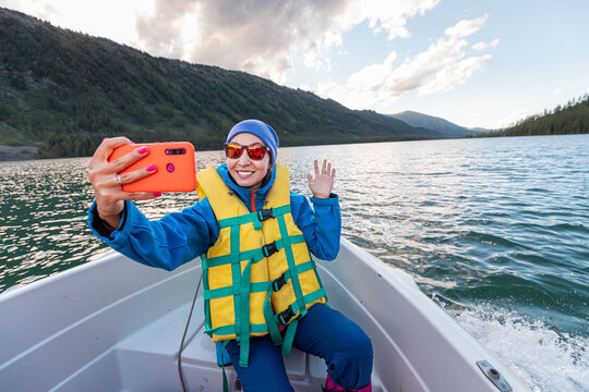 Happy woman in a life vest taking selfie photo in a boat on a mountain lake
