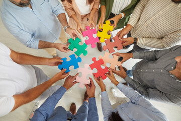 Team of creative senior and young business people joining pieces of colorful jigsaw puzzle as...
