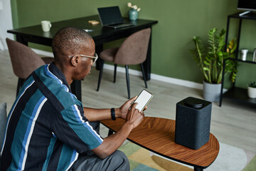 High angle view at modern black man connecting phone to smart speaker with voice controlled home AI