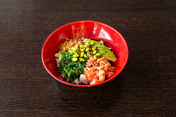 Large classic poke bowl of chopped Norwegian salmon with edamame beans, wakame seaweed, avocado, white rice, sesame and poppy seeds and crispy onion