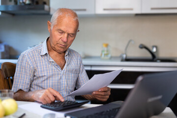 Old man sitting at table and counting with calculator
