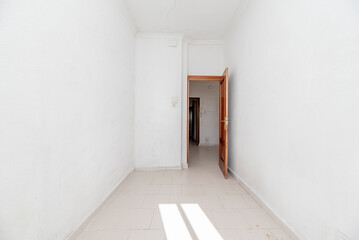 empty room with a mahogany colored door with white painted walls, sunbeams and white stoneware flooring