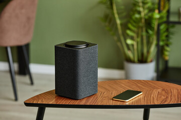 Minimal background image of smart speaker with home AI system on wooden table against green wall,...