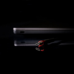 Fashionable black and red usb type-c plug next to a thin laptop or ultrabook. Black background....