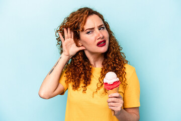 Young ginger woman holding an ice cream isolated on blue background trying to listening a gossip.