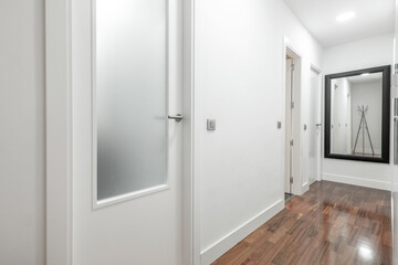 Hallway of a residential home with brown hardwood floors, pristine white walls, and a black-framed mirror