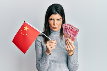 Young hispanic woman holding china flag and yuan banknotes skeptic and nervous, frowning upset because of problem. negative person.
